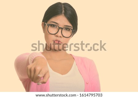 Studio shot of young Asian nerd woman pointing finger at camera