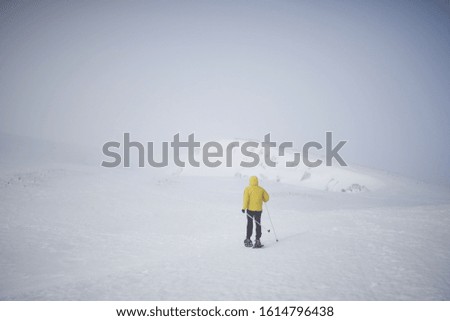Athlete man dressed in yellow walking through the snow with snowshoes, there is a lot of fog