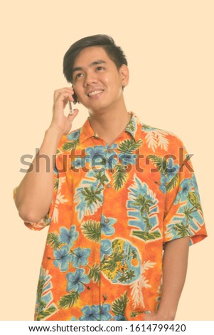 Young happy Asian man smiling and talking on mobile phone while thinking