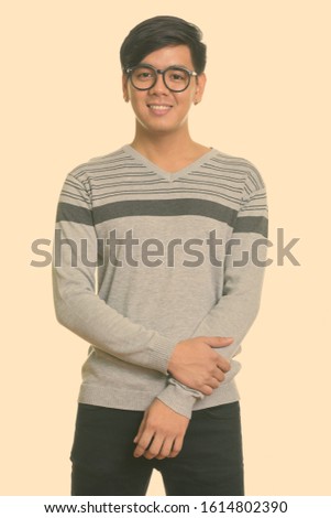 Studio shot of young happy Asian man smiling and wearing eyeglasses