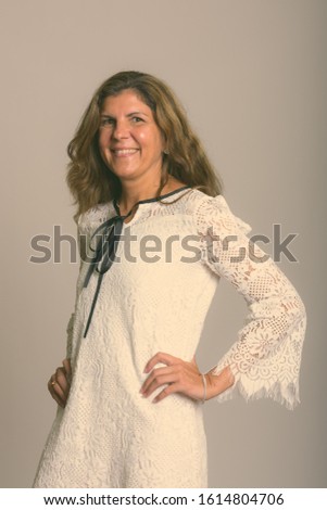 Studio shot of mature happy woman smiling and posing with hands on hips