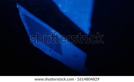 Bright blue painted wall surface closeup in black darkness. Uneven layer of glossy paint on wall in old building. Grunge abstract background of geometric shape shadow from window frames.