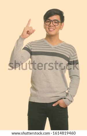 Studio shot of young happy Asian man smiling and pointing finger up