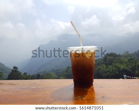 Iced Americano or Iced coffee  with Mountain view.Black coffee with ice in plastic glass. International food concept. Soft focus,Select focus