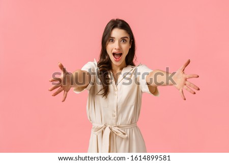Come into my arms. Excited beautiful caucasian girl stretching hands forward to hold, take something, cheerfully smiling, embracing friend, greeting girlfriend, heading shopping, pink background