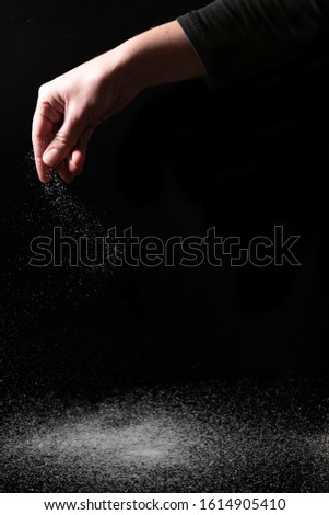 Creative image of hand scattering sugar powder on a dark background Royalty-Free Stock Photo #1614905410