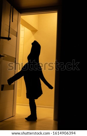 
A silhouette of a child in his father's sweater plays a ghost at home. Children silhouettein in the orange light.