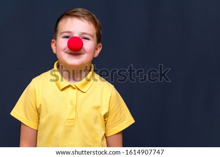 Funny teenager european boy with red clown nose looking at camera.Gray studio background.