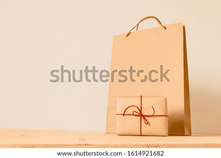 A gift rewound with red ribbon and a large paper bag on a wooden table.
Background gray.place for logo or design