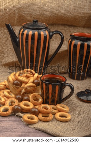 Small bagels, a mug of tea and ceramic dishes on a background of rough homespun fabric close-up.