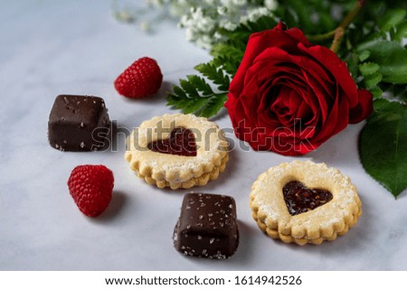 Raspberries with dark chocolate and heart shaped cookies. Red rose in the background.