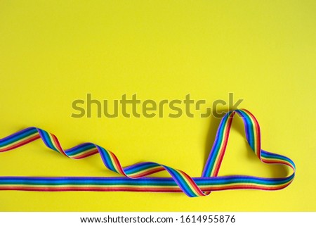 Heart made of rainbow ribbon on a yellow background. Pride concept