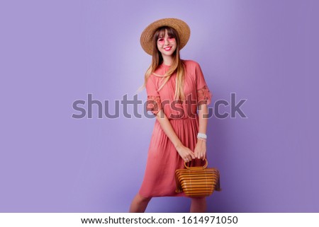   Studio photo of  pretty brunette woman in trendy  pink dress  and straw hat holding bamboo bag on violet background. Spring fashion look.  