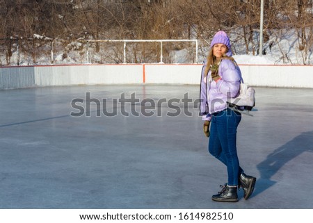 Lovely young woman with ice skates hanging on neck on the ice rink. Girl is going to skating on ice in a winter frosty day