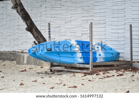 Sky Blue Kayaks, stored in the place made from metal on white sand beach next to the white wall, Vintage style.