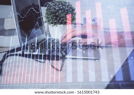 Multi exposure of graph with man typing on computer in office on background. Concept of hard work. Closeup.
