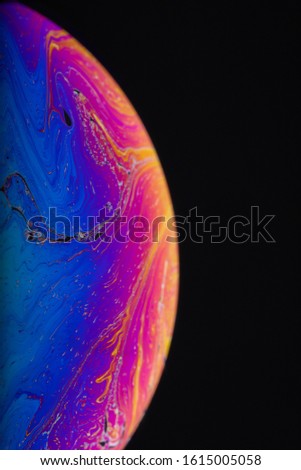 Close up macro photograph of the psychedelic rainbow of colors mixing and swirling in a soap bubble to look like a fantasy galaxy or planet isolated against a black background
