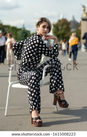 female lessons lifestyle outdoor posing on a summer day. beautiful caucasian model in a black suit with white spots in high heels, pants and a shirt. Long legs, bright makeup.