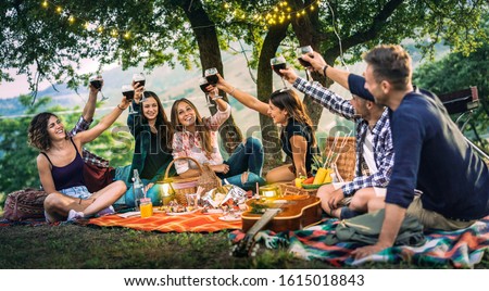 Happy friends having fun at vineyard on sunset - Young people millenial toasting at open air picnic under string light - Youth friendship concept with guys and girls drinking red wine at bar-b-q party