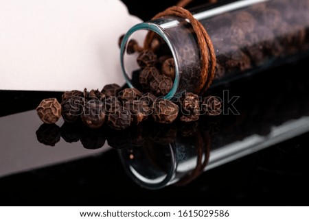 black pepper peas scattered next to the test tube and cork on a dark background