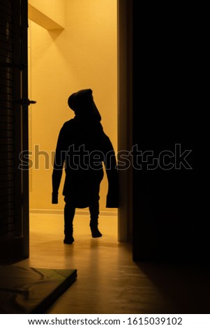 A silhouette of a child in his father's sweater on the yellow background. Children silhouettein in the orange light. Indoor.
