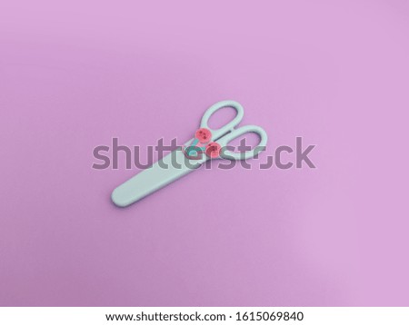 closeup mint green scissors closed with a childish cherry safety case isolated on lilac background