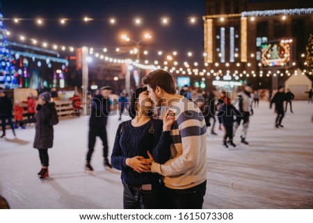 Young couple skates at the rink and kisses on the background of of evening city lights.