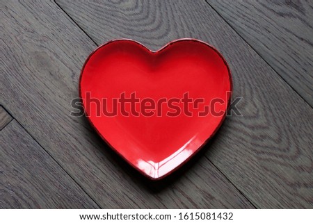 A red heart shape plate on dark wooden background. Decoration for Valentine's day, wedding, birthday of any other love celebration.