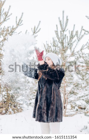 Portrait of a happy beautiful young woman throwing snow up and enjoying life in the winter forest against the background of fir trees. Human positive emotions concepts