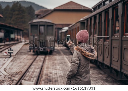 Tourist woman taking a photo with smartphone of side of vintage train on railway background