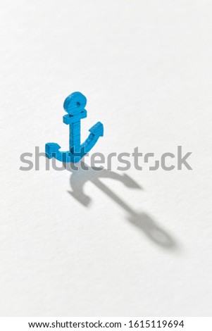 Long hard shadows on a ligth grey background from small blue plastic anchor toy with copy space.