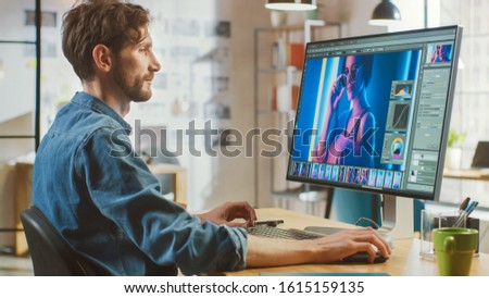 Beautiful Creative Male Video Editor with Beard and Jeans Shirt Works with Footage on His Personal Computer with Big Display. He Works in a Cool Bright Office Loft.