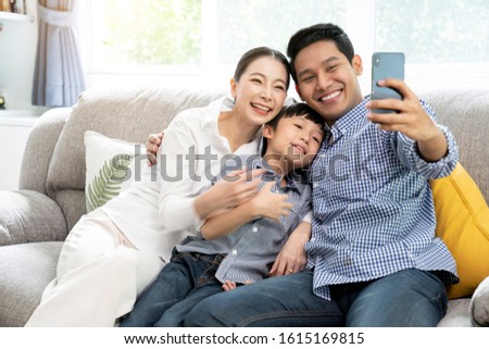Happy young Asian family taking selfie photo together by smartphone at living room