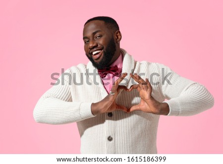 Handsome man shows heart symbol, shapes love sign with hands. Photo of african american man in love on pink background. Be my Valentine