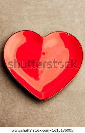 A red heart shape plate on grey concrete background. Decoration for Valentine's day, wedding, birthday of any other love celebration.