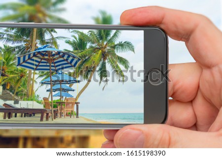Palm trees and tents on the ocean. Photo smartphone. Smartphone in hand. Landscape on monitor.