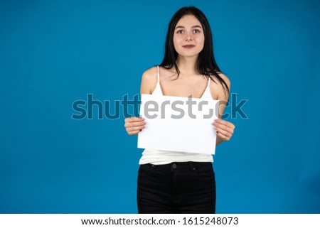 Front view of brunette girl holding blank paper and smiling isolated on blue background.