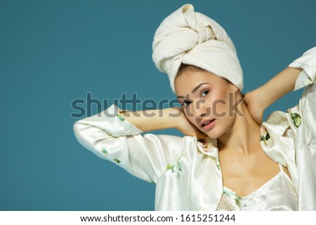 Cheerful attractive funny teen girl with towel on her head, over blue background. Morning beautiful young woman