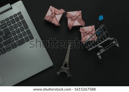 Online shopping. Laptop and gift boxes with bows, eiffel tower figurine on black background. Top view