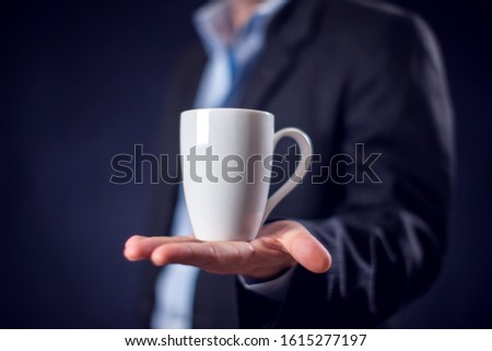 Businessman in suit holding cup of tea or coffee in hand in front of black background. Coffee break concept