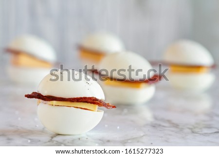 Keto BLT egg sandwich, or egg bun snack for the ketogenic diet plan. Boiled eggs with turkey bacon and cheddar cheese. Selective focus with blurred background.