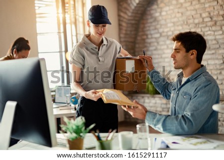 Smiling female courier delivering package to a businessman while he is working in the office. 
