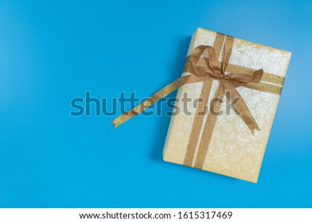 A gold or yellow gift box tied with glitter brown ribbon placed on blue background