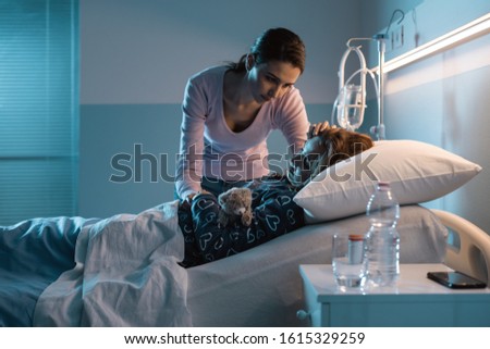 Young mother assisting her young child lying in a hospital bed at night, she is worried and caressing her head