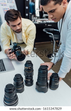 selective focus of handsome art director standing near photographer and looking at photo lenses