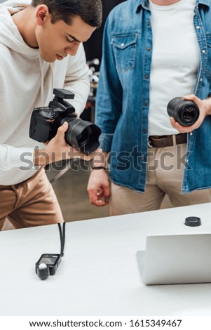 cropped view of art director holding photo lens near handsome photographer
