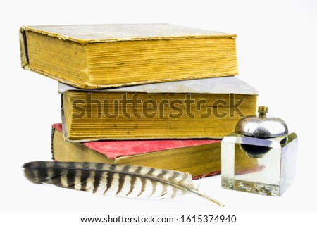 Three big old books, glass inkwell and colorful pen isolated on a white background.
