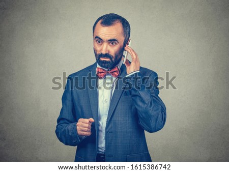 Businessman talking on a mobile phone listening to his voice messages with a serious expression on face. Mixed race bearded model isolated on gray grey background with copy space. Horizontal image