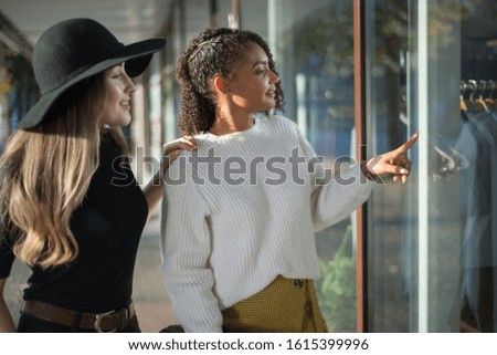 Portrait of a pair of beautiful Hispanic girls at the store counter. Girls point their finger at the counter with clothes. One of the women in a black hat. Fashion photography