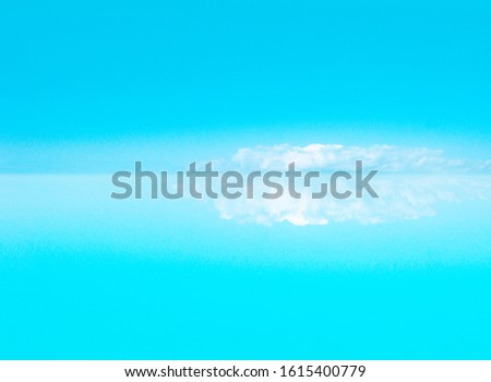 Water and sky, reflection of a large cloud in the water. The cloud is like an iceberg or snowy mountains. Calm background with copy space. Cyan sky and turquoise water.